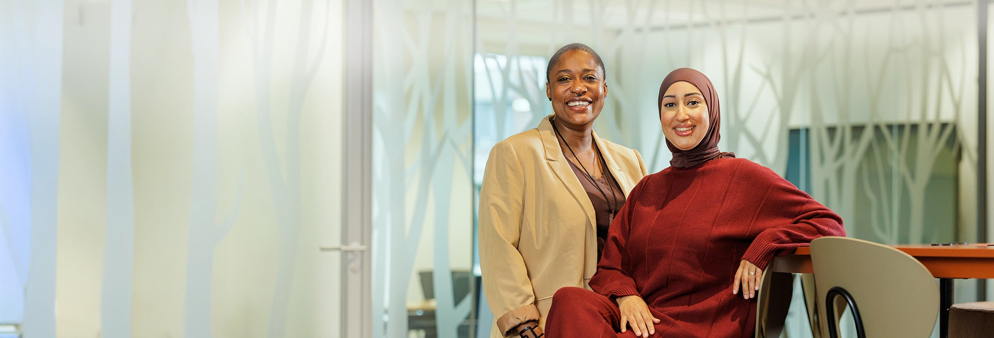 Decoratieve foto van twee vrouwelijke collega's van de Regionale Belasting groep, welke direct in de camera kijken.