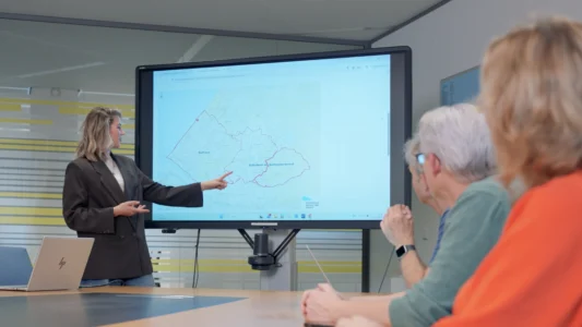 Decoratieve foto van meerdere collega's van de Regionale Belasting groep, welke allen kijken naar een presentatie van een vrouwelijke collega van de Regionale Belasting Groep.